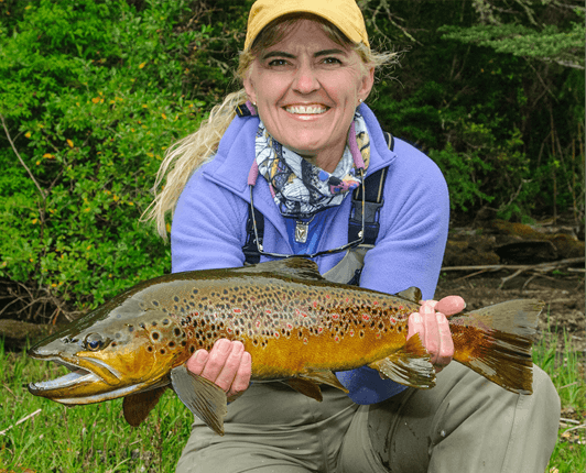 Woman kneeling, proudly holding a brown trout
