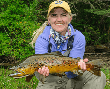 Woman kneeling, proudly holding a brown trout